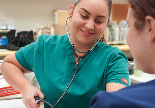 A medical assistant student practicing taking blood pressure on another student.