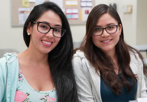 two smiling young women sitting together in class