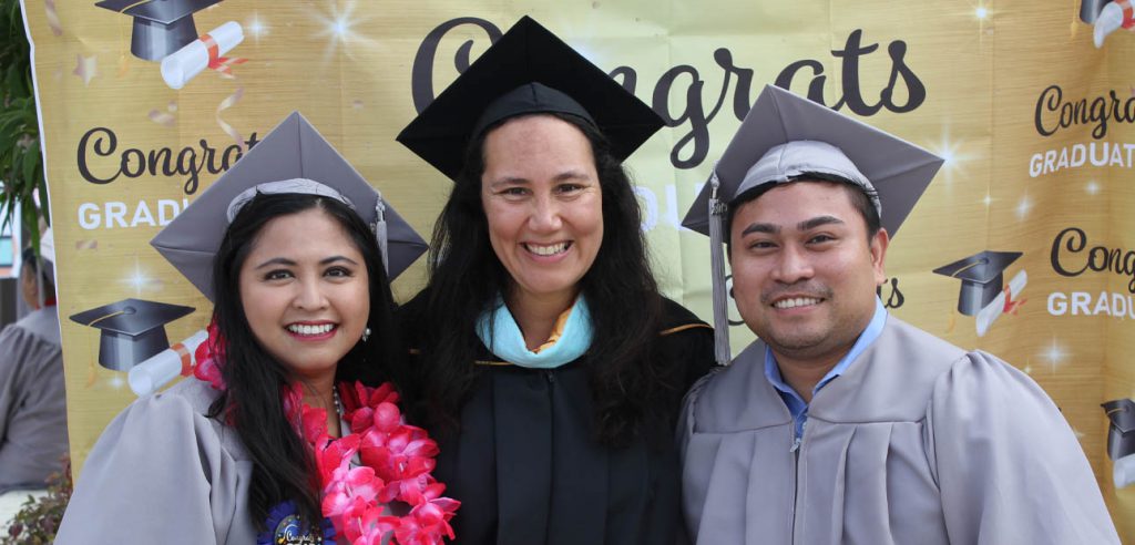 A photo of an NOCE counselor posing with two students in their cap and gowns