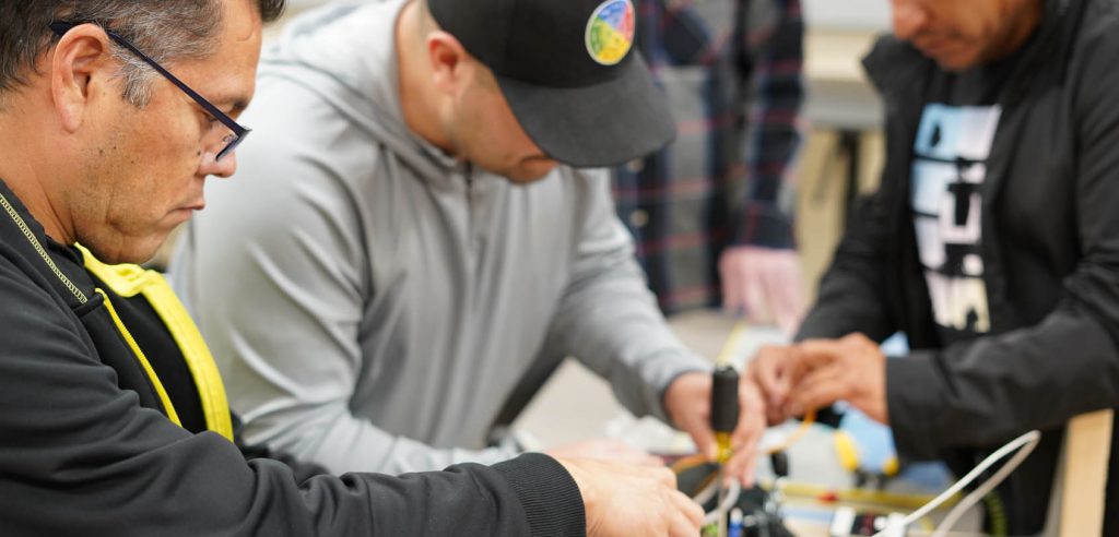A photo of two electrical students. One is securing the light switch and checking wires, while the other student is wiring the switch to the main electrical source of power.