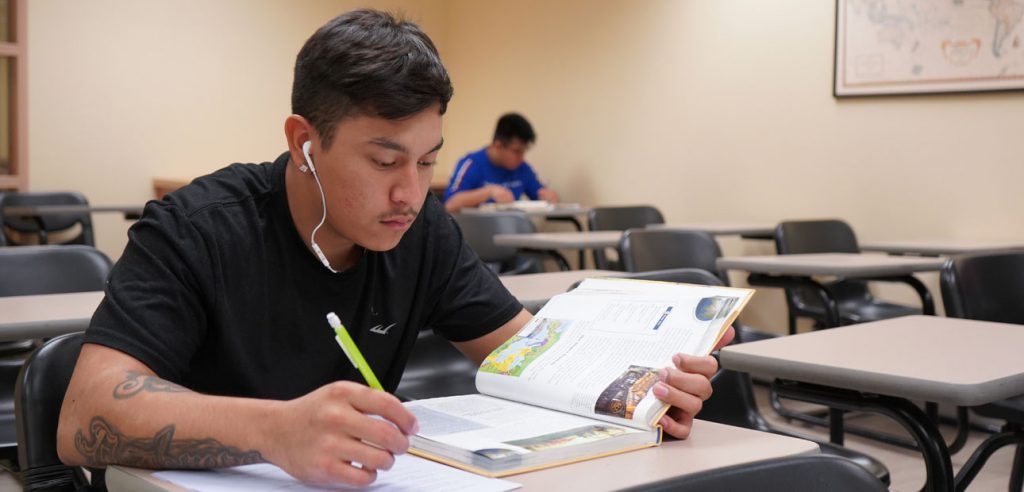 A photo of a student working on an assigment as, while he reads his textbook