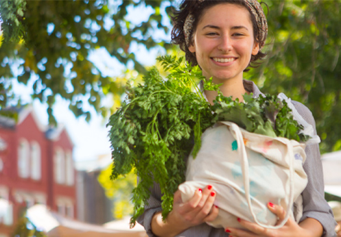 A smiling woman holding a canvas bag of vegetables