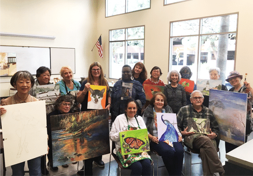 A group photo of the Older Adults' Painting class with everyone posing with their paintings.